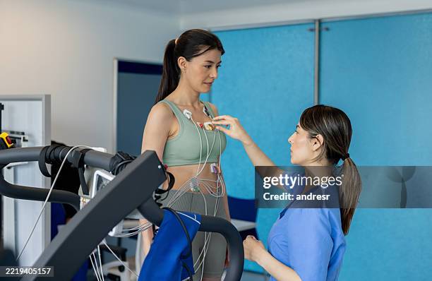 krankenschwester legt elektroden an eine frau, die in einer klinik einen belastungstest macht - belastungsprobe stock-fotos und bilder