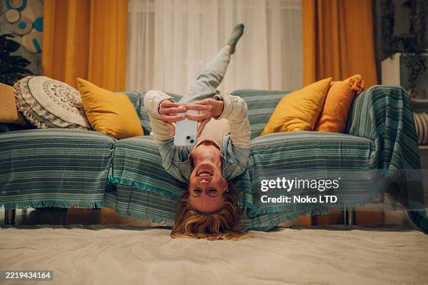 verspielte frau, die smartphone kopfüber auf dem sofa zu hause benutzt - auf-den-kopf-gestellt stock-fotos und bilder