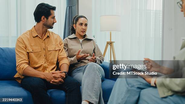 junges paar in ernsthafter diskussion mit psychiater während der eheberatungssitzung sitzt auf dem sofa im wohnzimmer zu hause. therapiesitzung konzept für psychische gesundheit. - eheberatung stock-fotos und bilder
