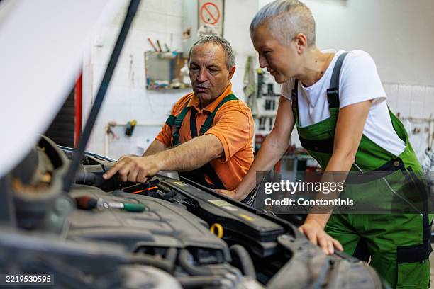 man helping his female colleague while working at auto repair shop - tradeswoman stock pictures, royalty-free photos & images