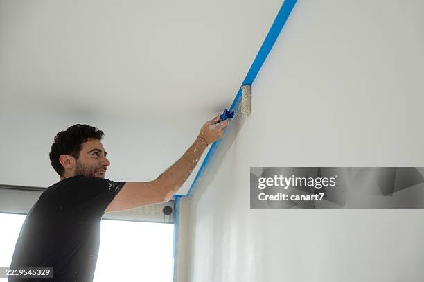 painter using roller brush, painting wall edge, home renovation - afplaktape stockfoto's en -beelden