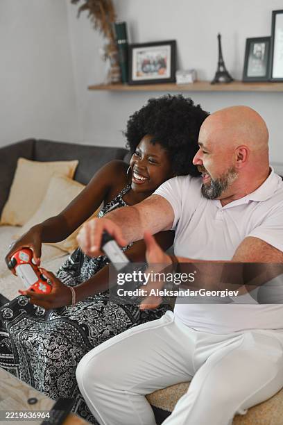 excited multiracial couple screaming with laughter while battling each other in video game - dating games stock pictures, royalty-free photos & images