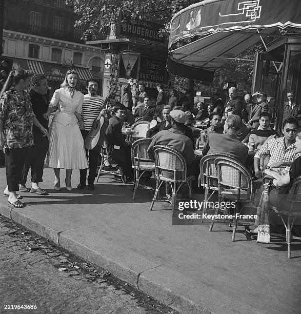 La chanteuse Catherine Sauvage et l'actrice Dany Robin sont debout, avec deux musiciens, à la terrasse du café des Deux Magots, lors d'une scène du...