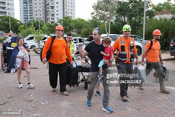 Man carries his son as they evacuate the area following a strike by an Iranian missile in the Israeli city of Petah Tikva, east of Tel Aviv, on June...