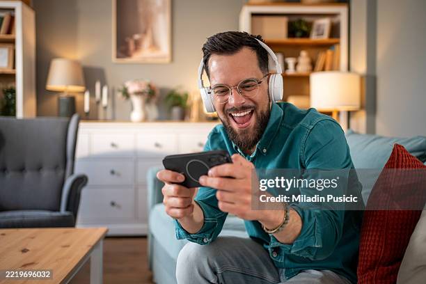 excited young man playing mobile video games at home - mobile game stock pictures, royalty-free photos & images