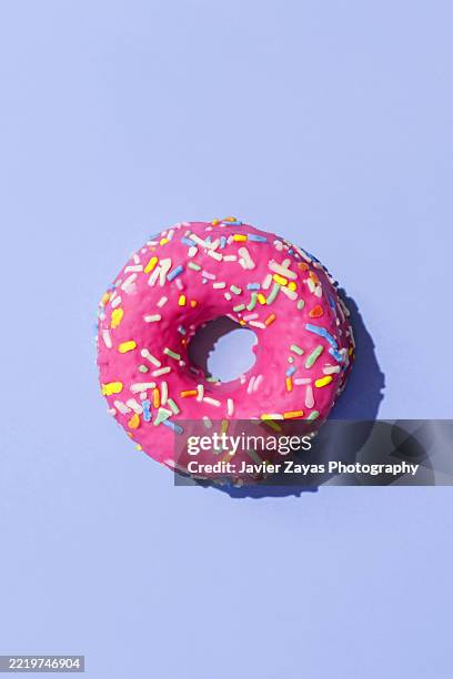delicious pink donut with colorful sprinkles on a vibrant purple background - doughnut stock pictures, royalty-free photos & images