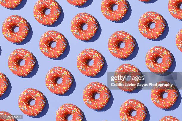 pattern of pink donuts with sprinkles on a purple background - doughnut stock pictures, royalty-free photos & images