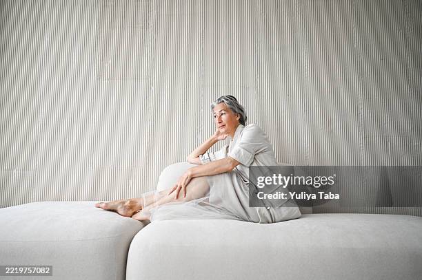 senior woman relaxing on comfortable sofa at home - midlife crisis stock pictures, royalty-free photos & images