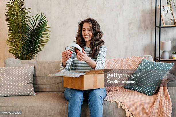 mujer joven desempaquetando un paquete con auriculares nuevos que ordenó en línea - paquete fotografías e imágenes de stock
