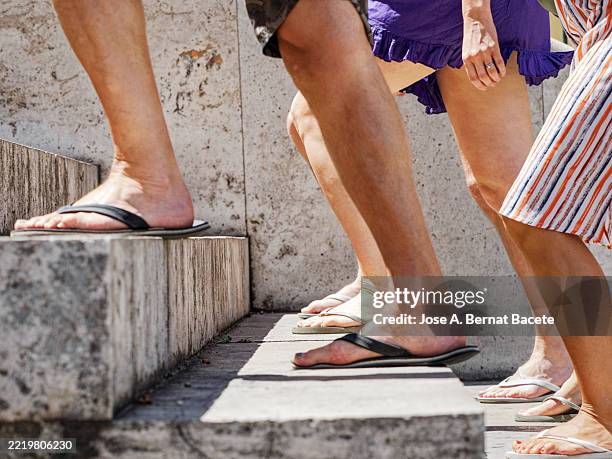 feet of young women and men wearing sandals and rubber flip-flops climbing a staircase in summer. - ciabatta infradito foto e immagini stock