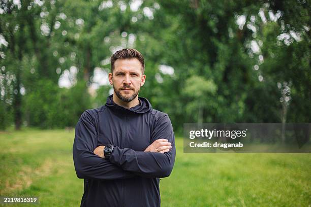 confident male athlete posing with crossed arms in lush green park - male likeness stock pictures, royalty-free photos & images