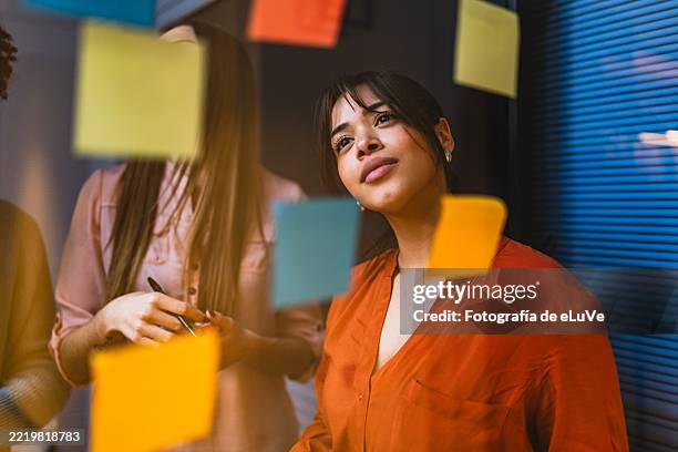 focused businesswoman reading notes on glass wall during brainstorming session - idée photos et images de collection