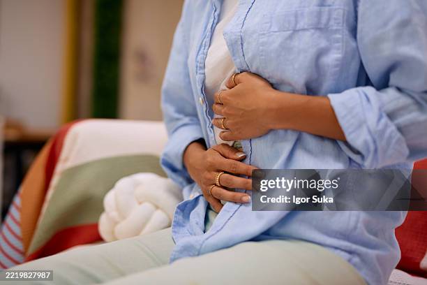 mujer que experimenta dolor abdominal mientras está sentada en la cama - hernia fotografías e imágenes de stock