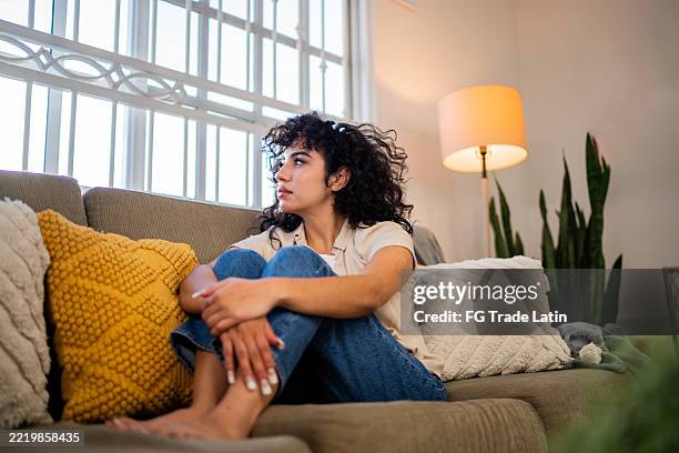 sad young woman looking through the window at home - verlegen stockfoto's en -beelden