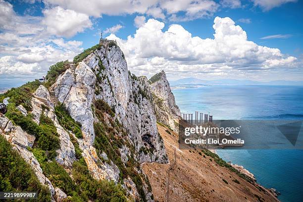panoramic view of gibraltar rock rising against bright sky, white clouds floating over azure mediterranean waters, highlighting dramatic landscape - headland stock pictures, royalty-free photos & images