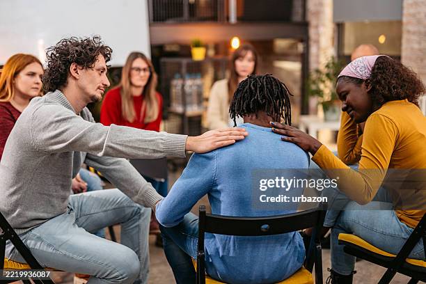 support group therapy patients consoling a young male patient at the group therapy indoors - substance abuse stock pictures, royalty-free photos & images