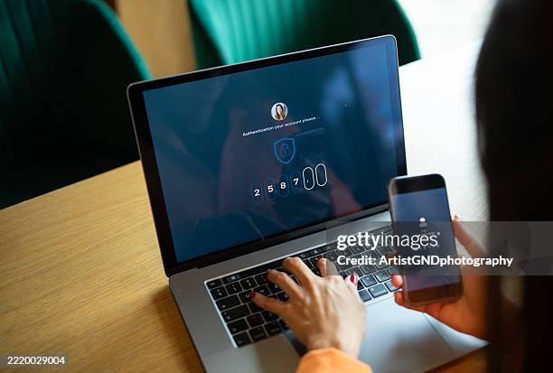 asian woman authorizing her identity by entering code from her phone to log in to her laptop. - digitale authenticatie stockfoto's en -beelden