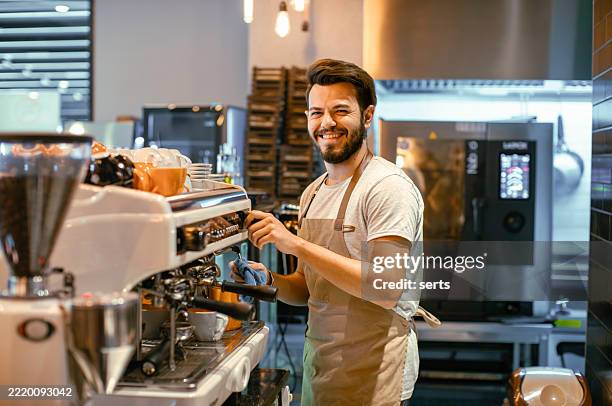 lächelnder junger barista, der kaffee an einer modernen espressomaschine im café zubereitet - barista stock-fotos und bilder