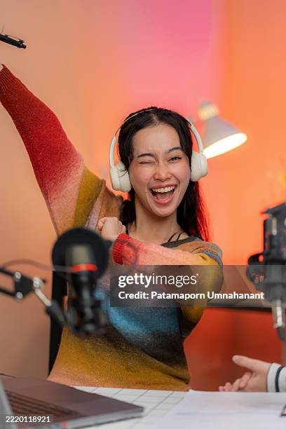 a cheerful podcast presenter celebrates gaining more followers with a bright smile and raised hand while speaking into a microphone. the scene captures the joy of digital success and engaging with audiences in a modern studio setup. - locutor-de-rádio imagens e fotografias de stock
