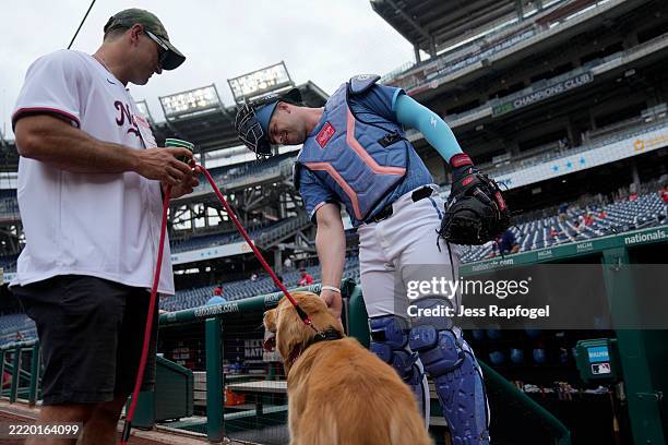 Riley Adams of the Washington Nationals pets Bruce the Bat Dog before a game against the Miami Marlins at Nationals Park on June 14, 2025 in...