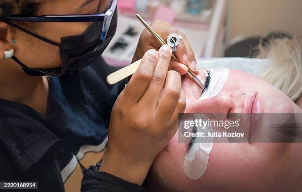 latina lash technician applying eyelash extensions to 31-year-old blonde client in beauty salon. - beauty spa stock pictures, royalty-free photos & images