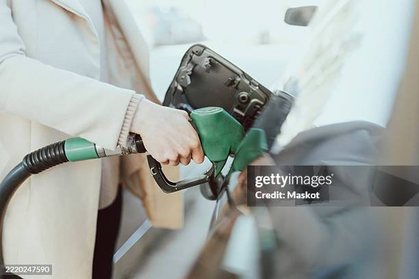 midsection of woman refueling car at gas station - bomba de combustible fotografías e imágenes de stock