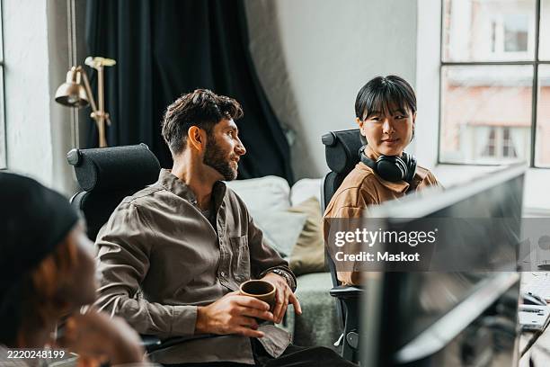 female computer programmer talking with colleagues sitting at tech start up office - programmer team stock pictures, royalty-free photos & images