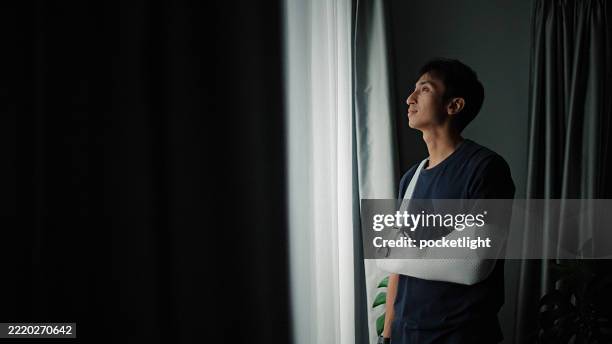 man with arm cast looking out window. - bone fracture stock pictures, royalty-free photos & images