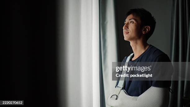 mann mit gipsarm, der aus dem fenster schaut. - knochenbruch stock-fotos und bilder