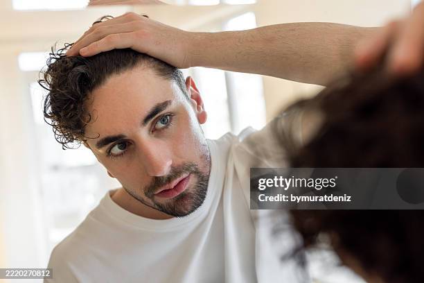 homme vérifiant ses cheveux devant le miroir - main dans les cheveux photos et images de collection