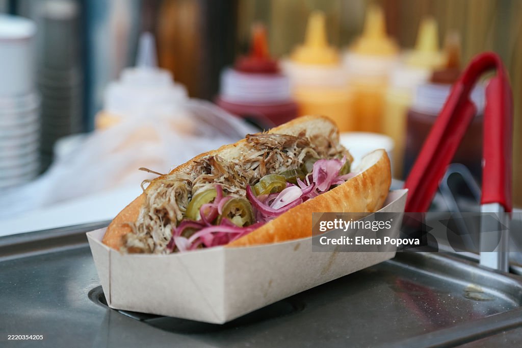 Hot Dog Bun With Chopped Beef, Pickles And Red Onion Against Ketchup And Mustard Sauce At The Street Market