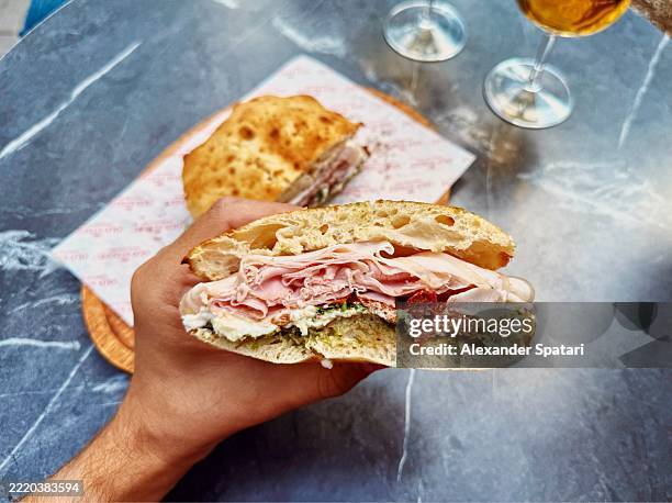 eating italian panino sandwich with prosciutto cotto and sun dried tomatoes, personal perspective view - panini stock pictures, royalty-free photos & images