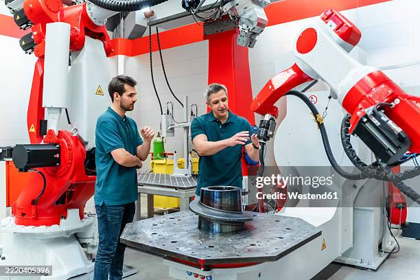 mature male engineer explaining automatic welding torch to colleague in factory - automatic welding torch stock pictures, royalty-free photos & images