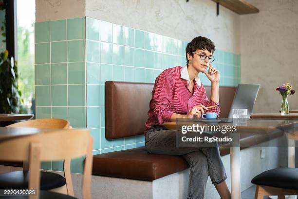 young woman working remotely from a coffee shop using laptop - all shirts stock pictures, royalty-free photos & images