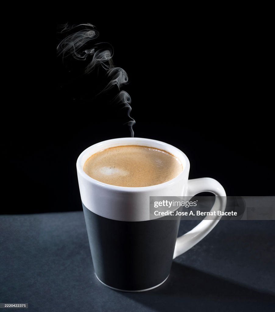 Cup of hot steaming coffee with milk on a black background.