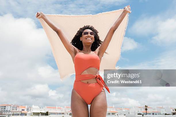 smiling woman wearing sunglasses holding beach towel on sunny day - peach bath towels stock pictures, royalty-free photos & images