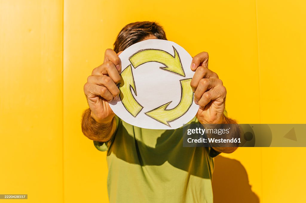 Man holding recycling symbol in front of yellow wall