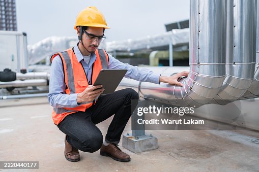 Technician using a tablet for diagnostics while inspecting industrial pipes at a plant Technician using a tablet for diagnostics while inspecting industrial pipes at a plant