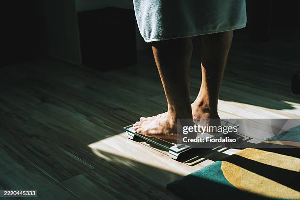 person weighing themselves on a scale in a sunlit home - balance photos et images de collection