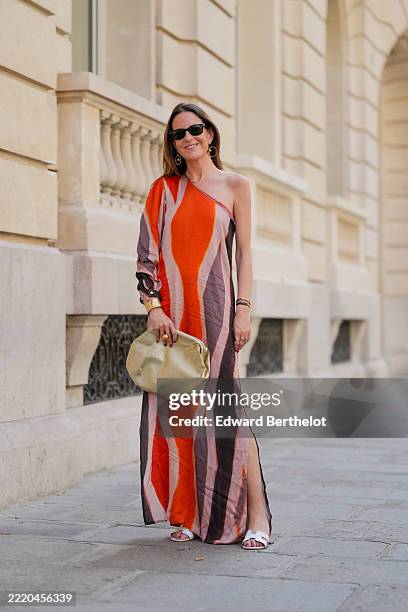 Alba Garavito Torre wears an asymmetrical, one-shoulder dress featuring bold vertical stripes in shades of orange, pink, and brown from Dragon Girl...