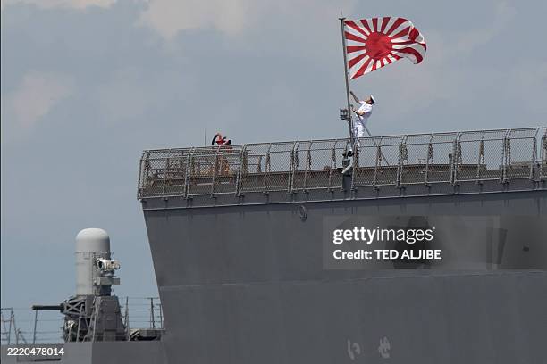 Sailor raises the Japan Maritime Self-Defense Force ensign on board the JS Ise, a Hyuga-class helicopter destroyer, as it docks at the international...