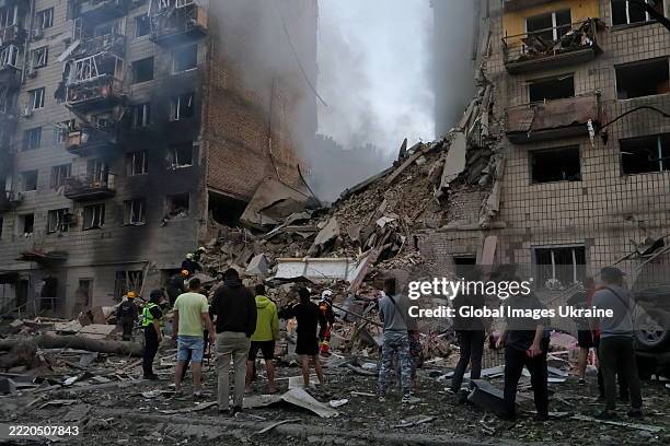 People gather near a nine story residential building in Solomianskyi district, where an entire building's section from the 1st to the 9th floor was...
