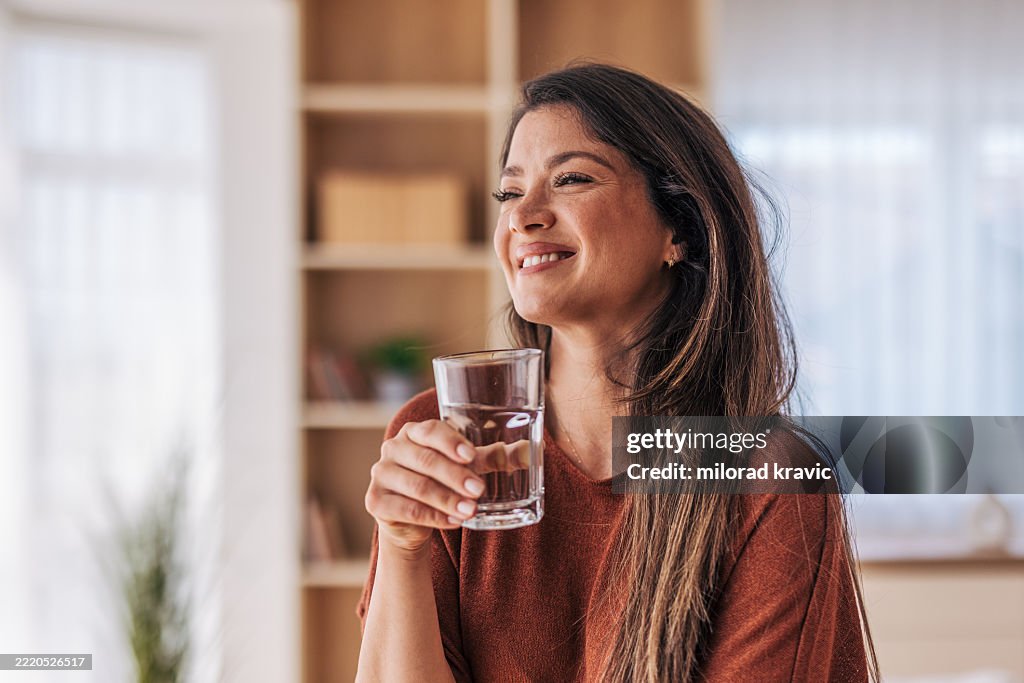 Schöne Frau, die zu Hause ein Glas frisches Wasser trinkt