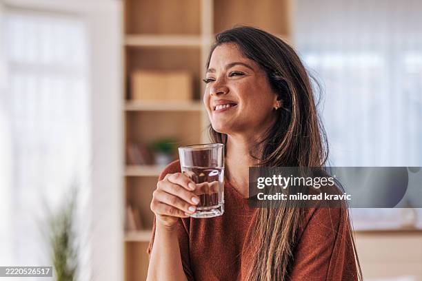 schöne frau, die zu hause ein glas frisches wasser trinkt - wasser trinken stock-fotos und bilder