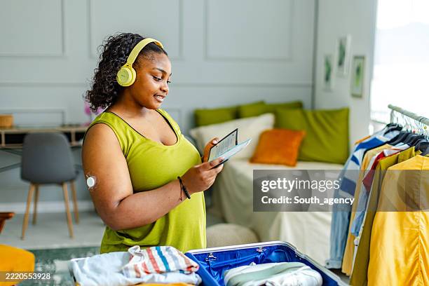 young black woman managing diabetes while packing for a trip in a stylish room - glucose stockfoto's en -beelden