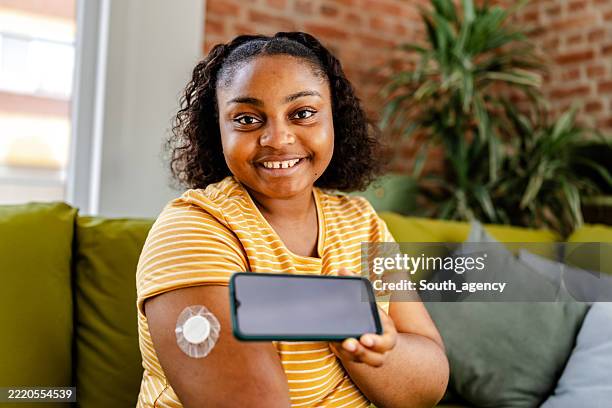 young black woman managing type 1 diabetes at home while using a smartphone for her health monitoring - continuous glucose monitor stock pictures, royalty-free photos & images