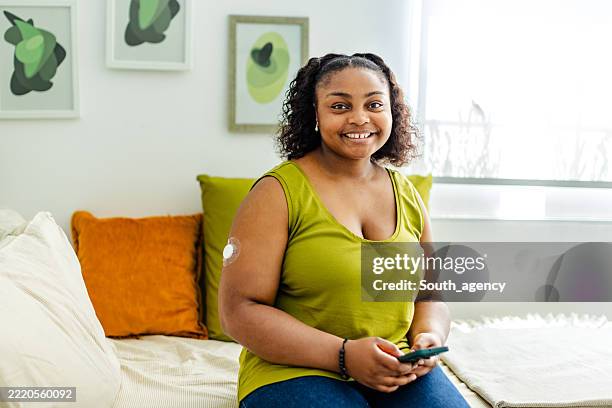 young black woman managing type 1 diabetes while sitting comfortably in a modern living room setting during the day - type 1 diabetes stock pictures, royalty-free photos & images