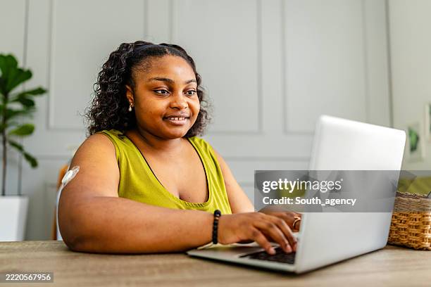 young woman with type 1 diabetes managing her health while working on a laptop at home - continuous glucose monitor stock pictures, royalty-free photos & images