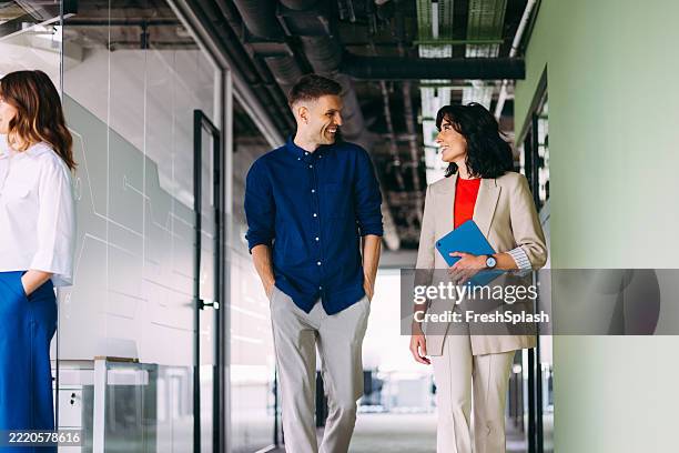 professional colleagues engaged in conversation walking through a modern office hallway - happy colleagues doing team building activity imagens e fotografias de stock
