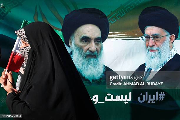 An Iraqi woman walks past a portrait of Iraq's top Shiite cleric Ayatollah Ali al-Sistani and Iran's supreme leader Ayatollah Ali Khamenei during...